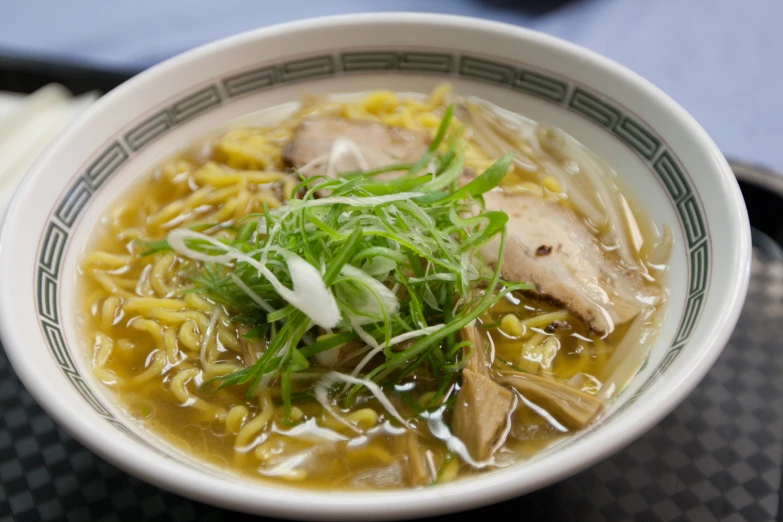 a bowl of chicken noodle soup with spring onions