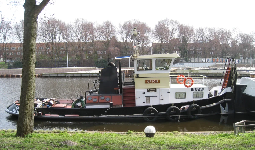 a tug boat with people standing on a dock near a tree