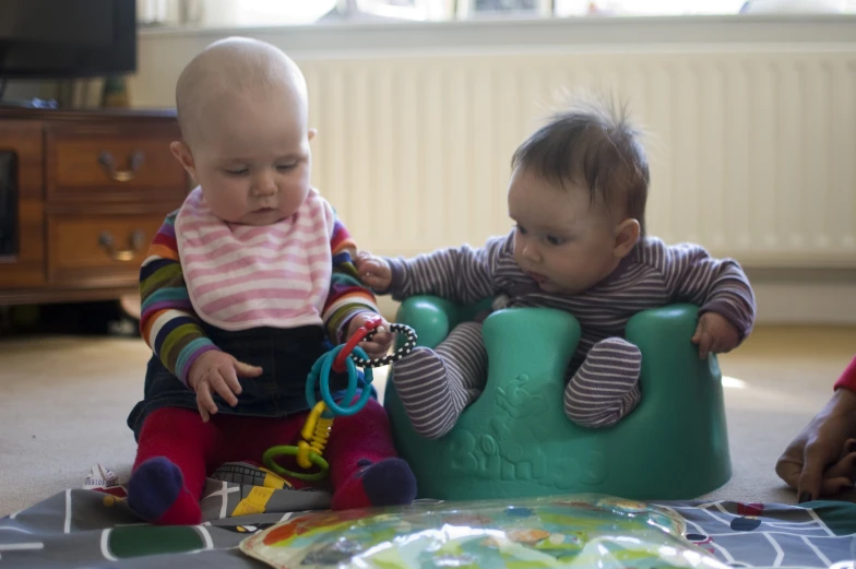 two babies play with their toys on the floor