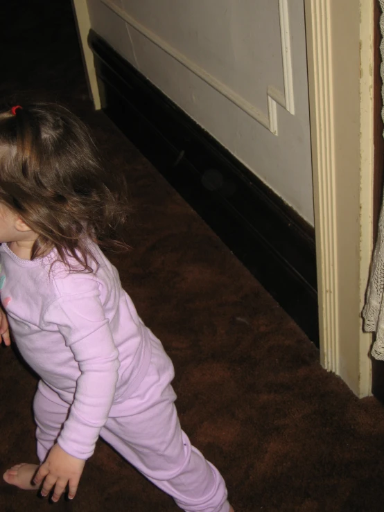 a little girl with brown hair in pink pajamas looking up