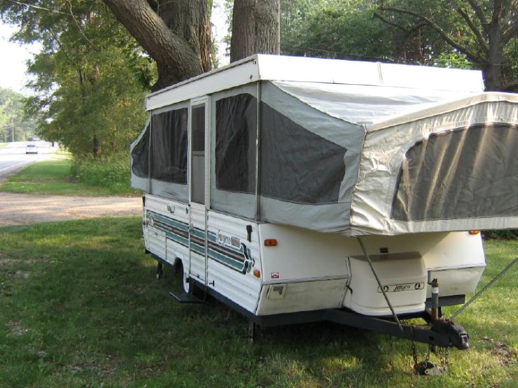 an rv trailer sitting in the grass in the shade