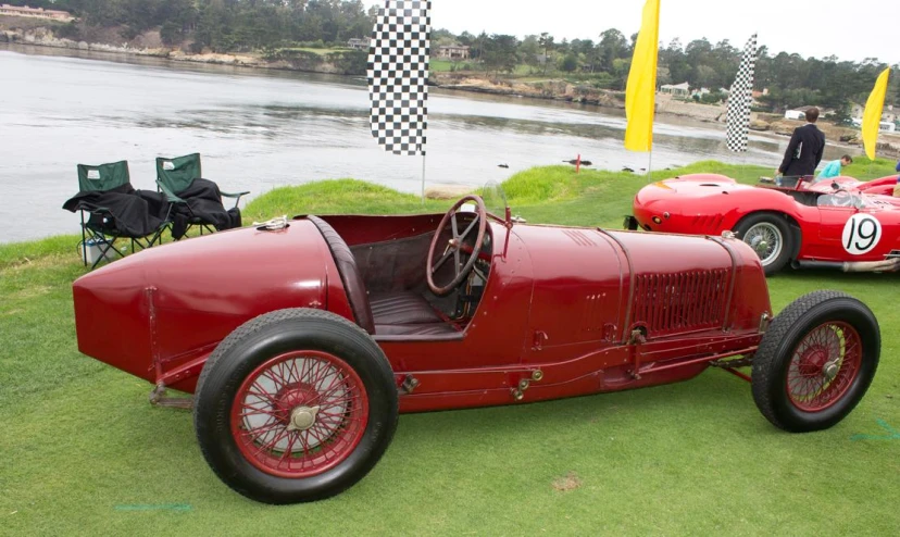 a classic car sits in the grass by a lake