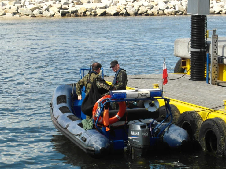 two men in an inflatable raft are loading equipment into the water