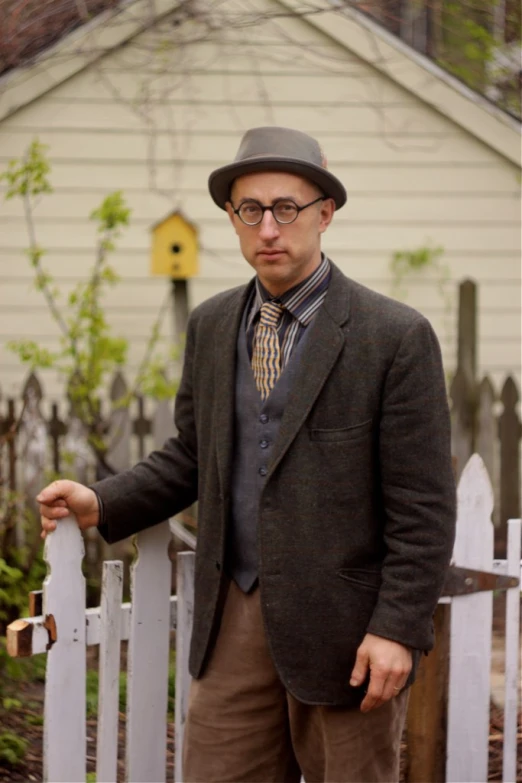 man in suit and tie standing near a picket fence