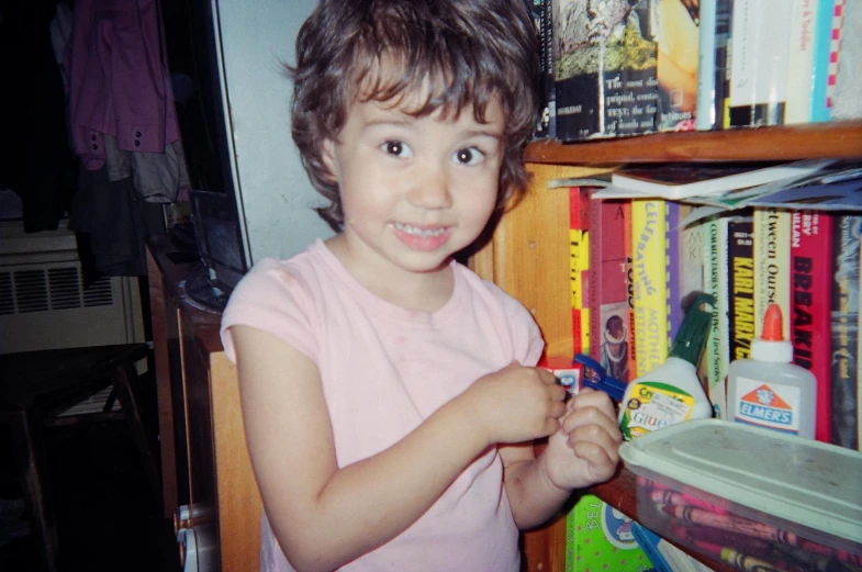 a young child holds up an object in front of a bookshelf