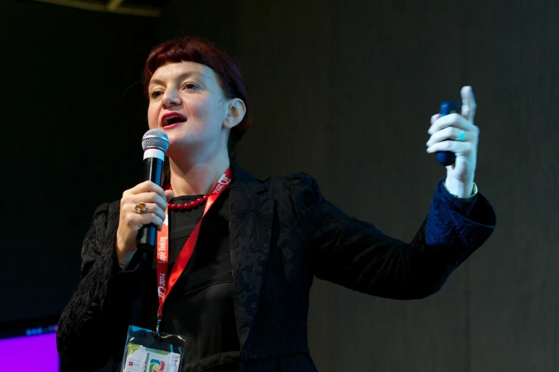 a woman talking into a microphone with a cellphone