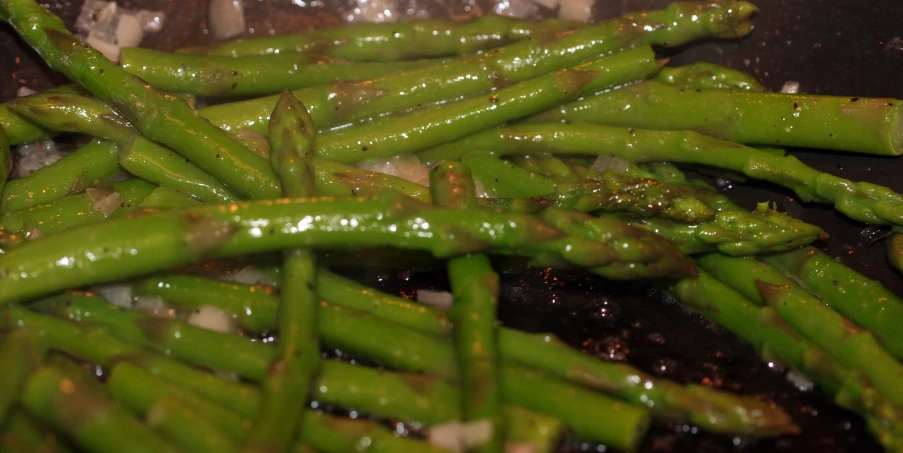 asparagus spears covered in brown oil on top of a black pan