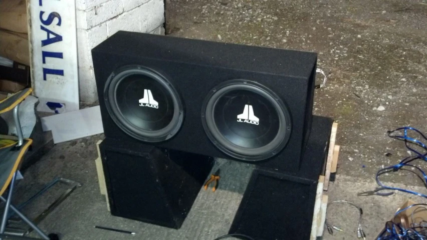 two black speakers sitting side by side on top of a box