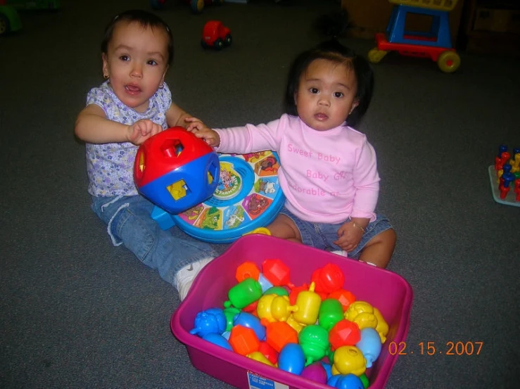 two little babies playing with toys on the floor