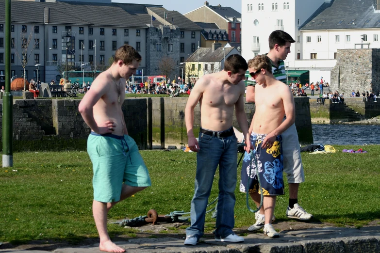 three young men standing in a park near a body of water