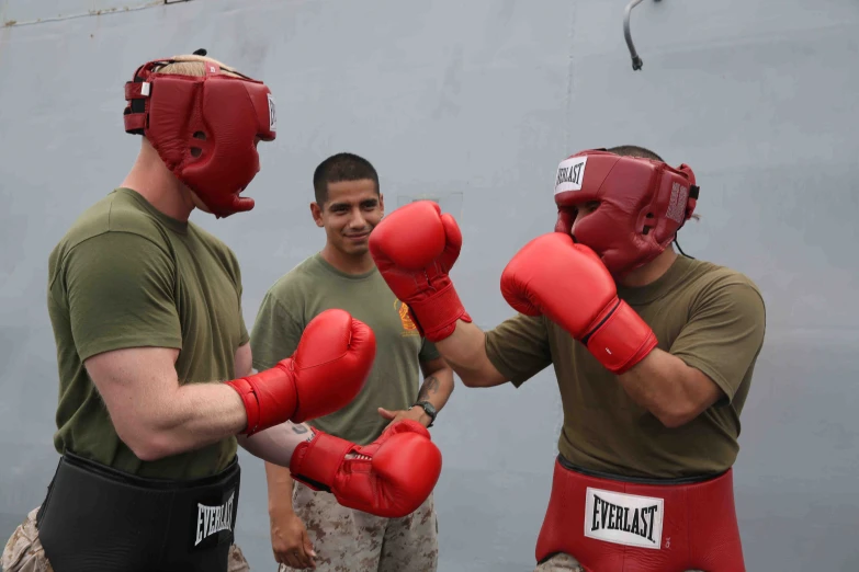 two men wearing red boxing gloves and green shirt stand close to each other, talking