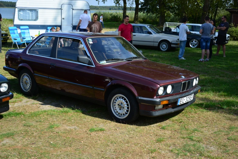 a maroon car parked in the grass near some people and cars