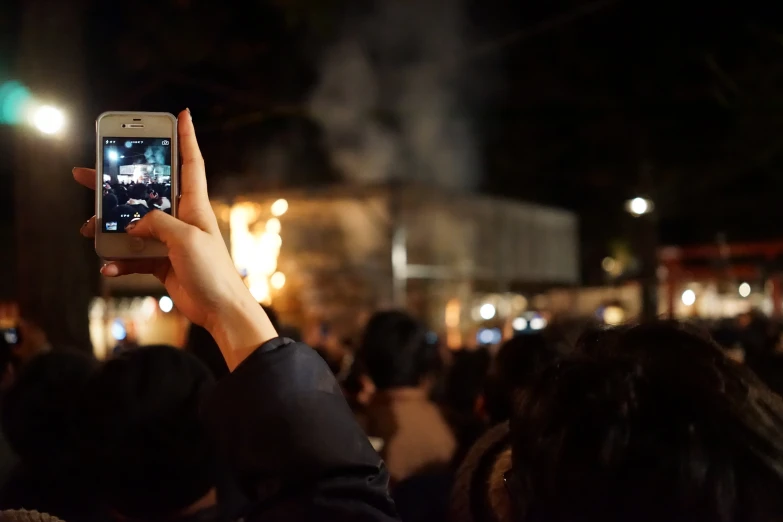 people standing at an outdoor concert are holding their cell phones up