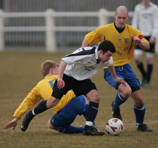 three soccer players vie for a ball during a game