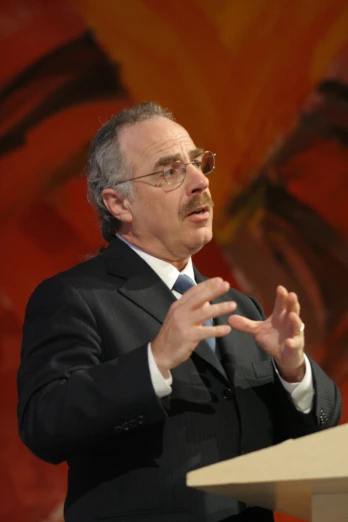 man with eye glasses and suit talking on stage