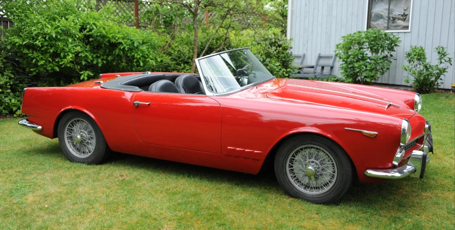 an old red sports car parked in the grass