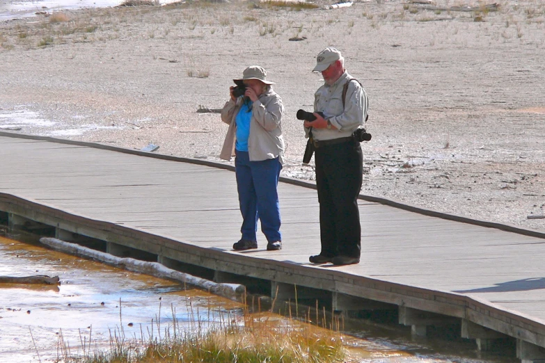 two people standing on a pier taking pictures with camera