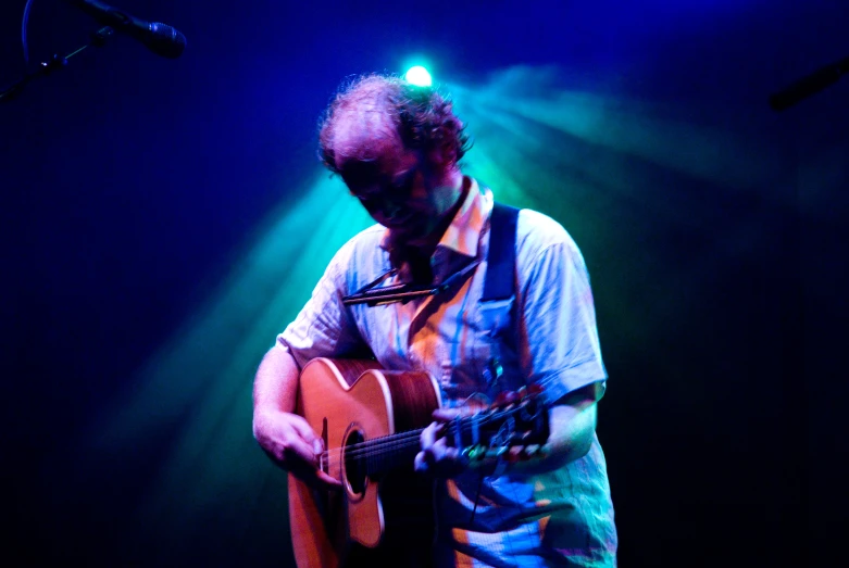 a man in blue shirt playing guitar in front of microphones