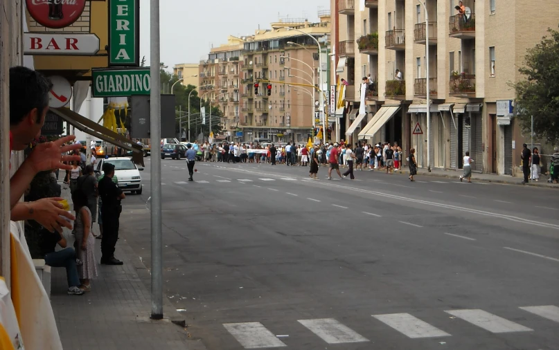 an empty street with people standing and sitting on the sidewalks