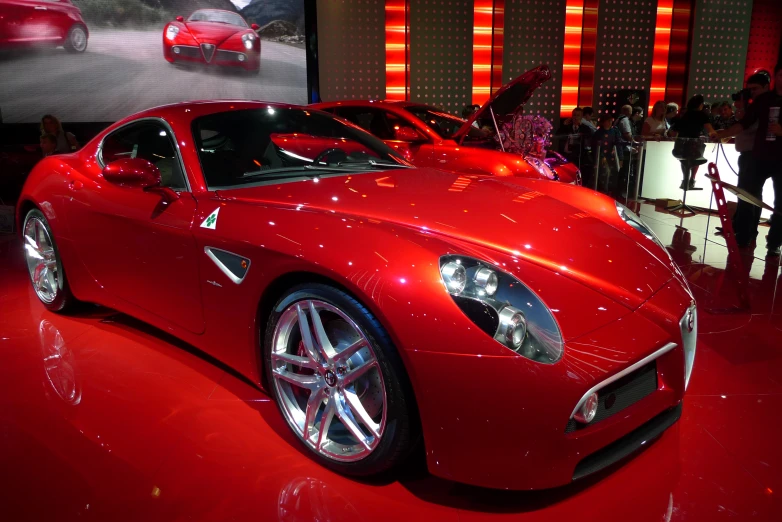 red sports car on display in front of a large screen