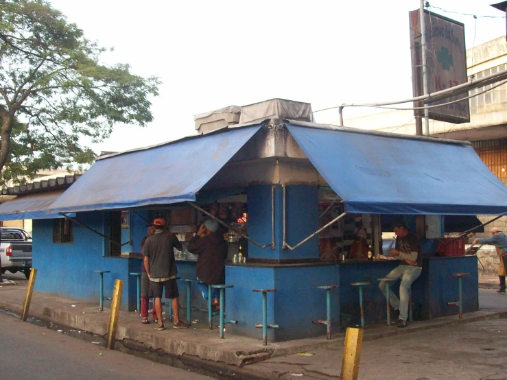 men are standing outside a blue building with two awnings