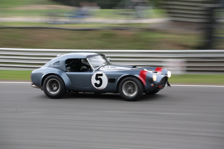 an old blue sports car speeds down the road