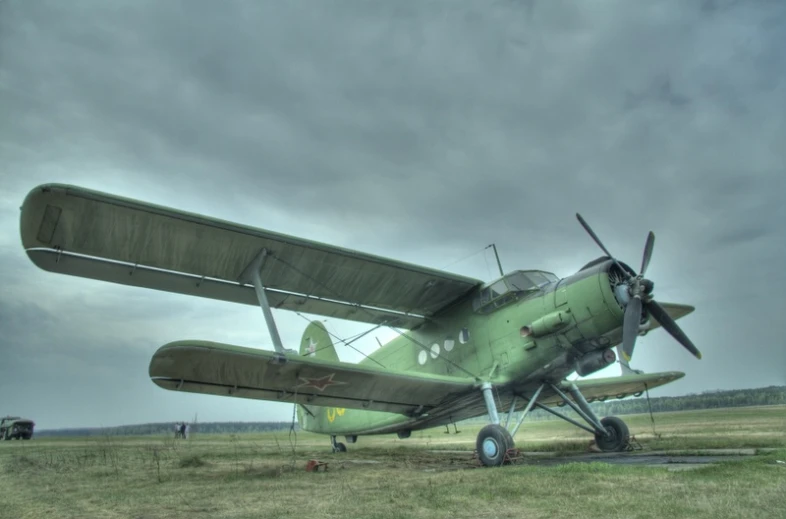 an old green plane is parked in the middle of the field