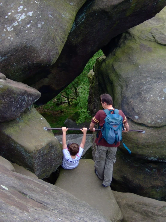 two people with their backpacks crossing a bridge over some rocks