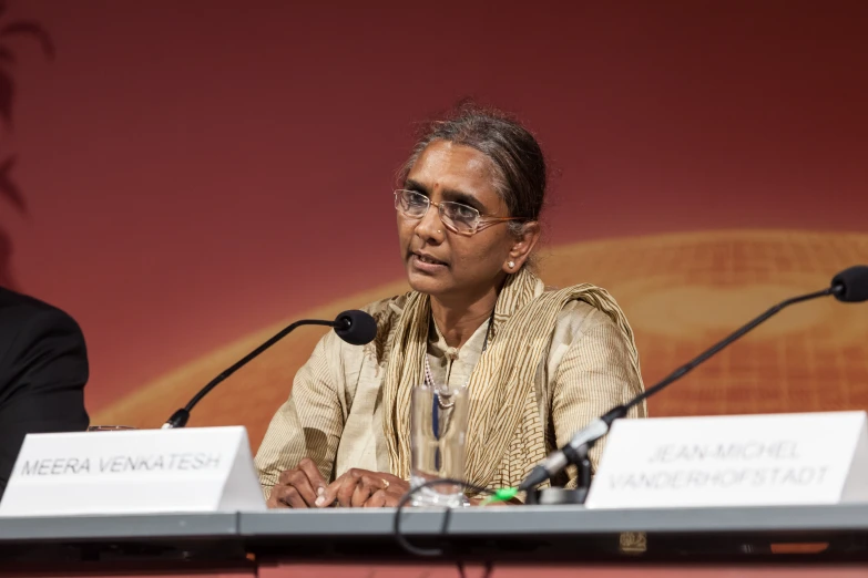 a woman sitting at a table with microphones behind her