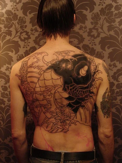 a man has an elaborate back tattoo of an asian demon and fish