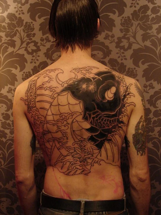 a man has an elaborate back tattoo of an asian demon and fish