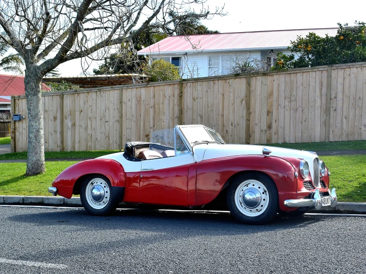 an old classic sports car parked in the driveway of a residential neighborhood