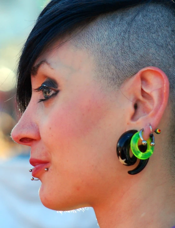 a person with a shaved head wearing colorful earrings