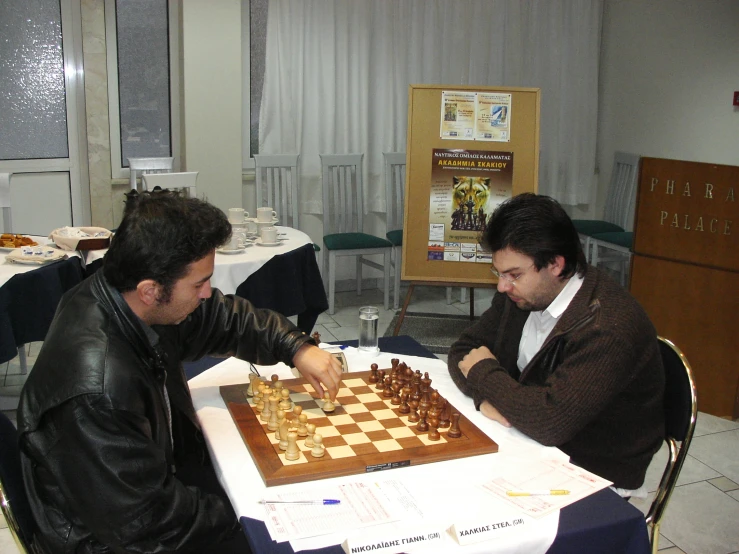 two men play chess at a dining room table