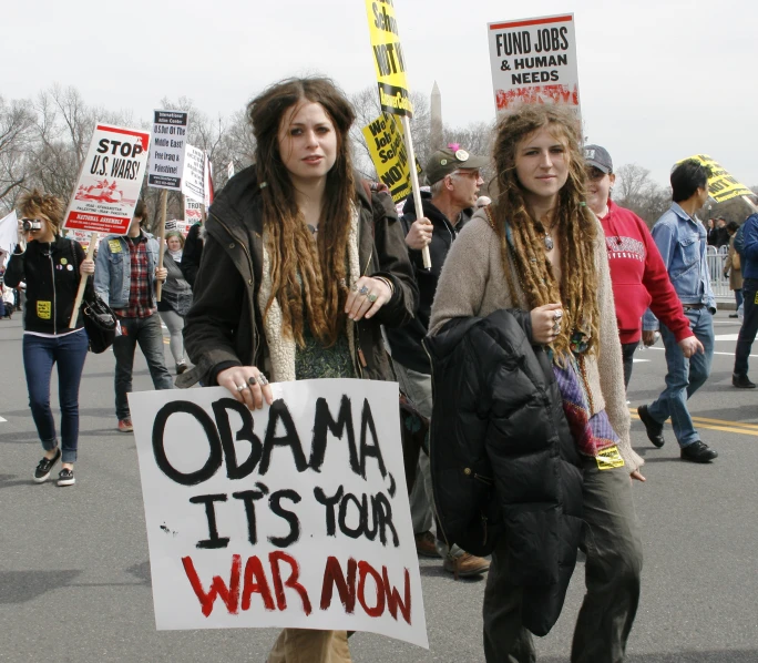 two people holding signs that read obama its your war on