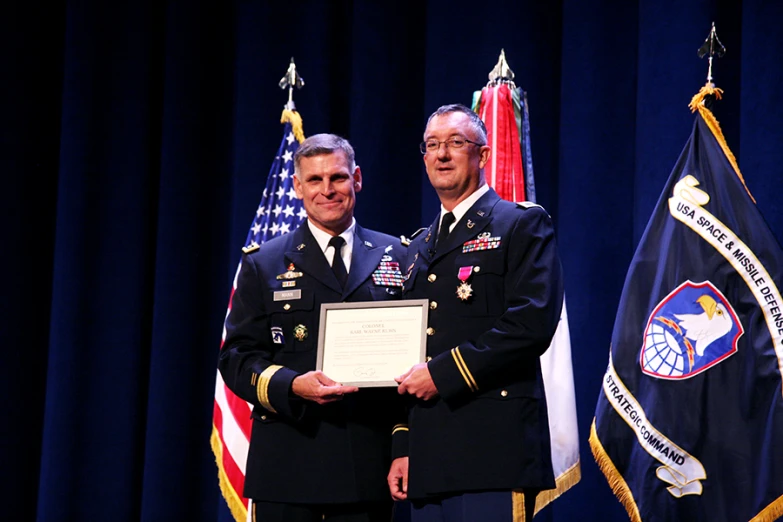 two men wearing military uniforms standing together holding a plaque