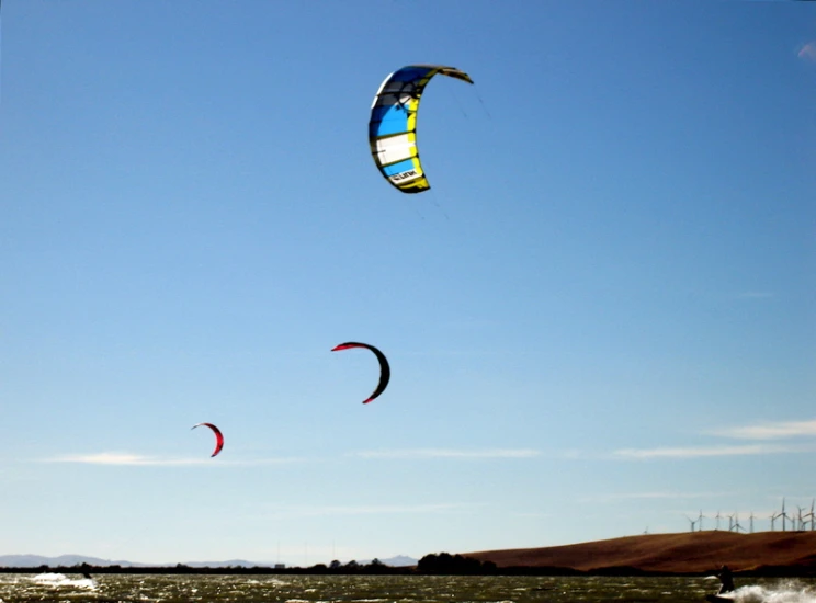 two parachutes flying in the blue sky over water