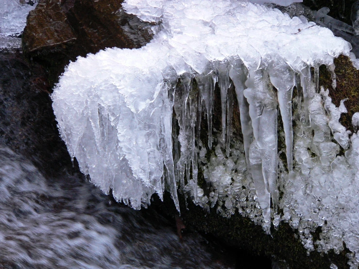 icicles are hanging from the top of a cliff near a stream