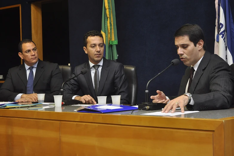 three men wearing suits and ties at a table with papers