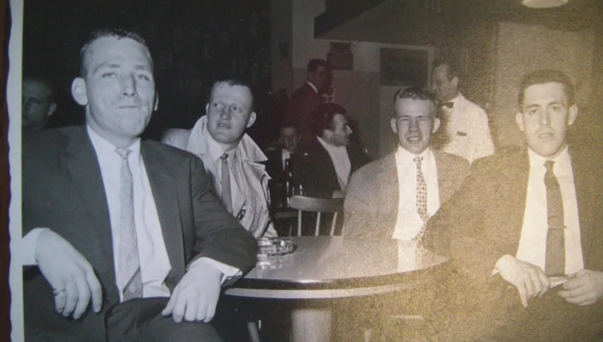 old pograph of men sitting at table in front of a wall