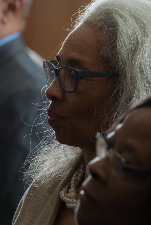 a woman wearing glasses and a suit stands near other people