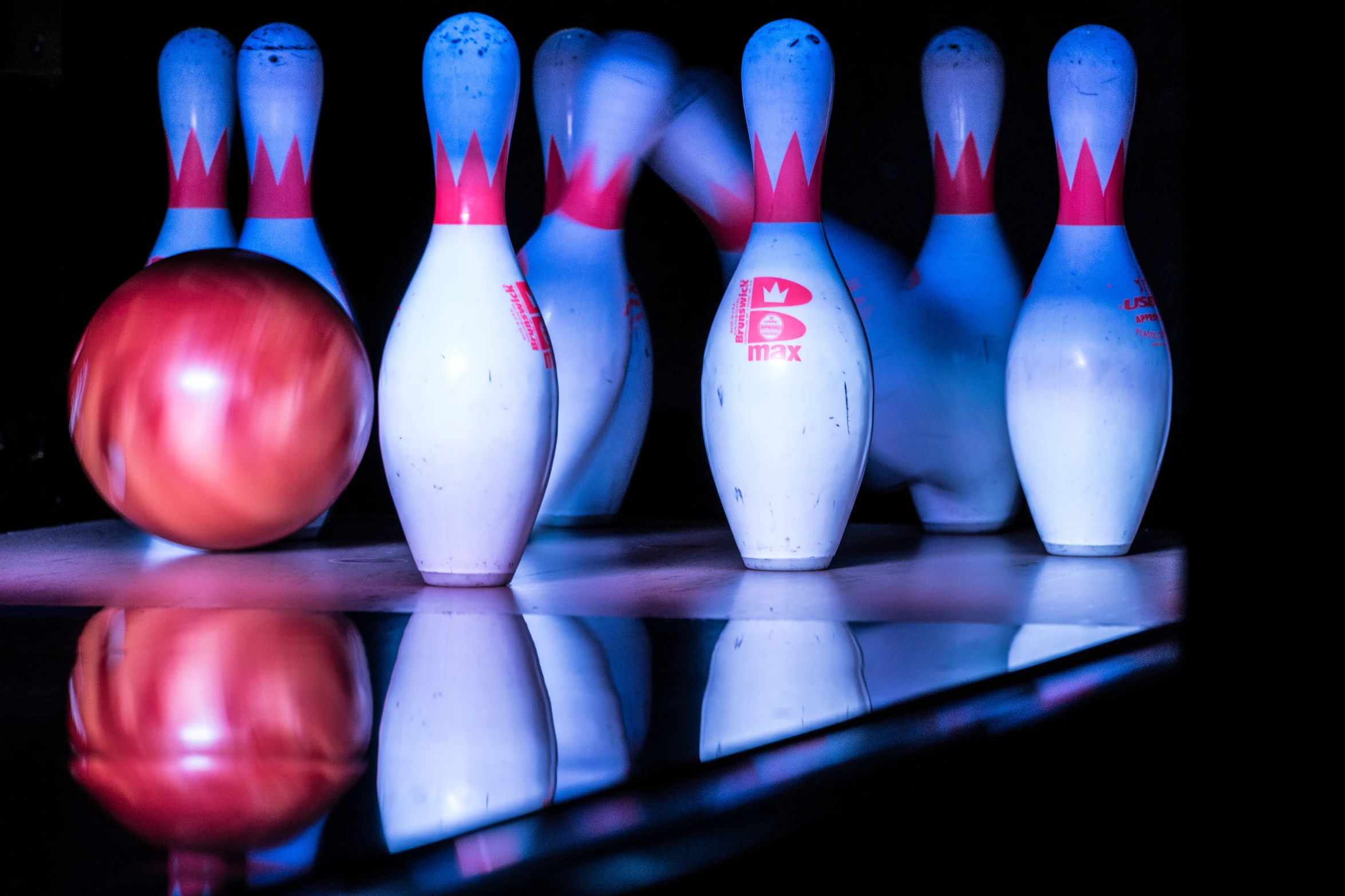 a bowling ball and four pins sit on a reflective surface