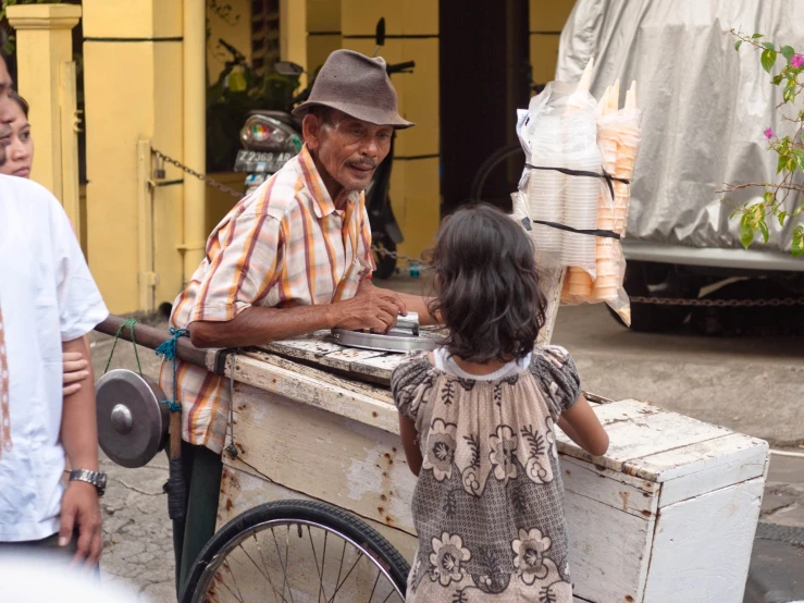 a man sells food from a cart, while  plays with her bike