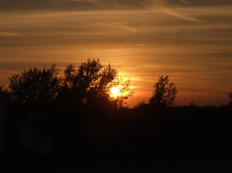 a sky with the sun setting behind some trees