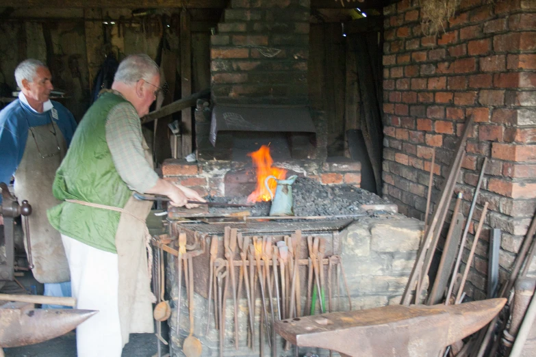 two elderly men standing near a brick fire oven with flames