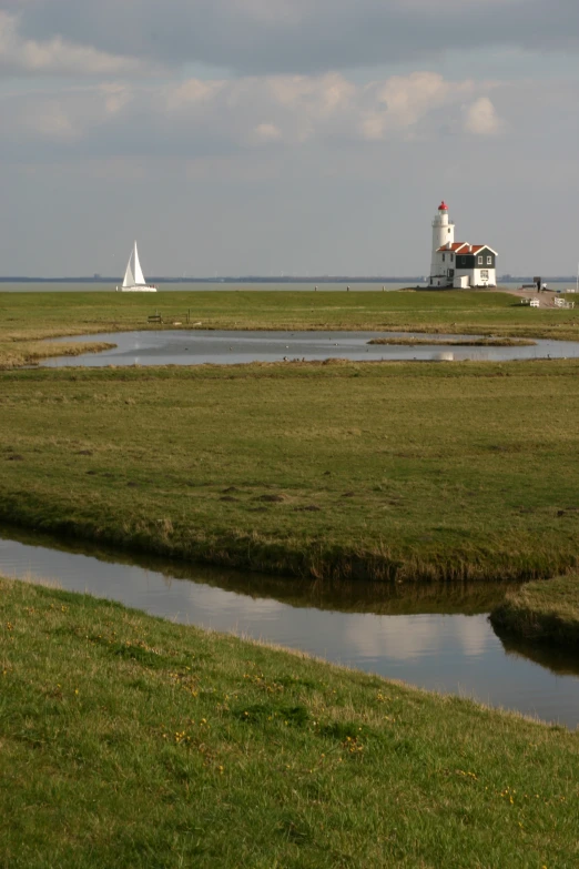 lighthouse with sail boats in the distance and small lake