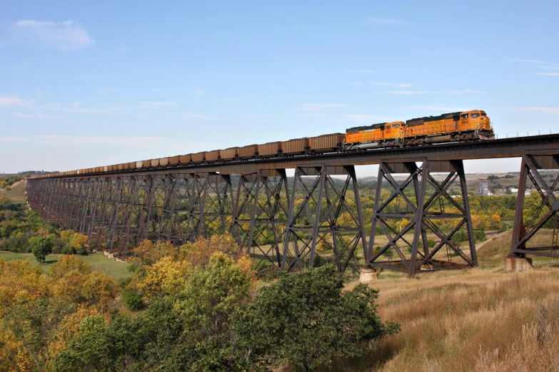 an orange train riding on top of a metal bridge