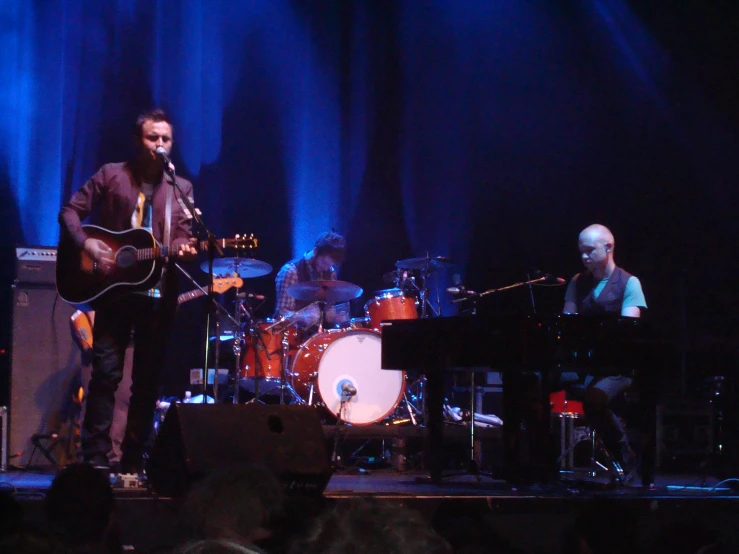 a musician on stage next to two other people