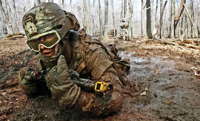 a man in camouflage clothing kneels and adjusts his goggles