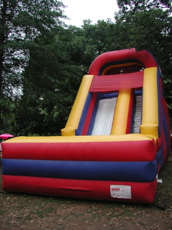 an inflatable slide sits on the ground next to a large tree